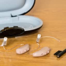 Close up of hearing aids with their case and a cleaning brush.