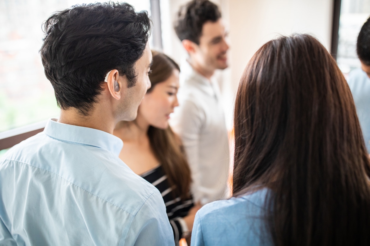 Young man with a hearing aid socializing with friends at a party.